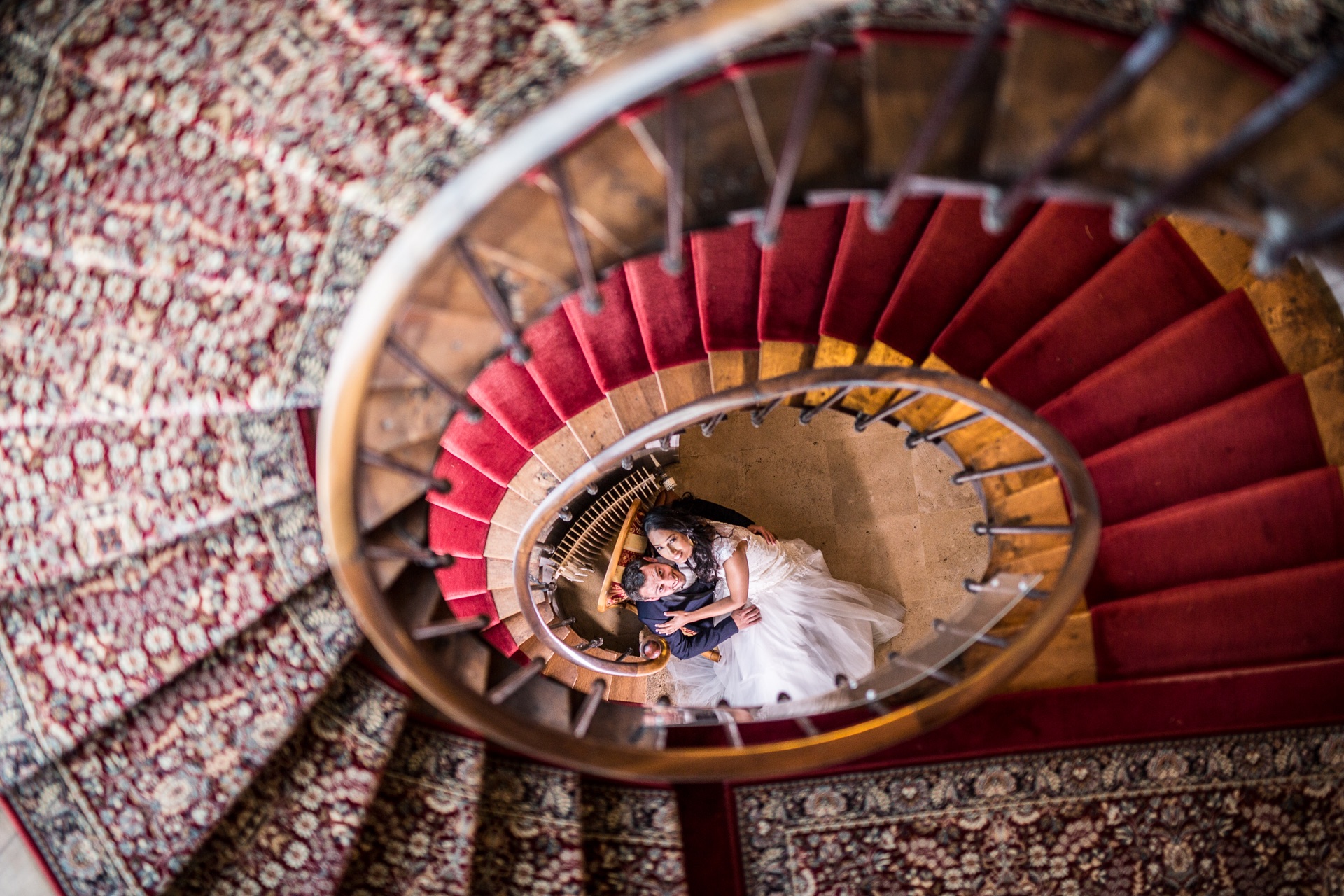 Mariés vus du haut dans un escalier aux tons rouges