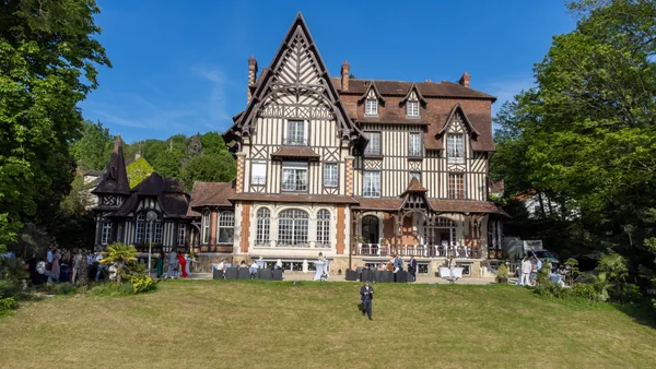 Façade à colombages du Domaine de Montmanoir, avec les invités sur la terrasse et le parc au premier plan